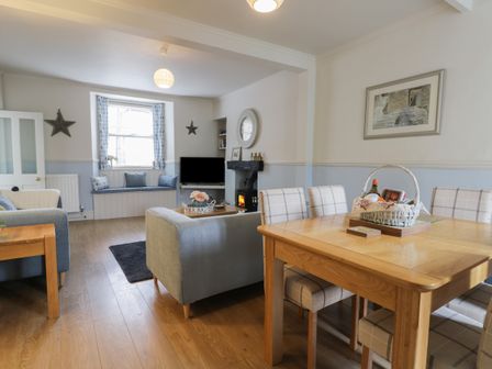 A dining area with a wooden table and chairs beside a living room with sofas a tv and a window seat at Potter Hill Cottage in Pickering