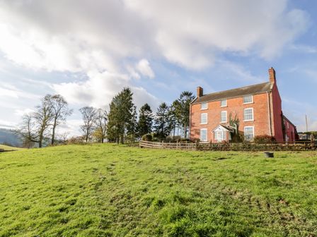A three-story brick house with a fenced garden on a grassy hill with trees at Squires Rest in Llanfair Caereinion