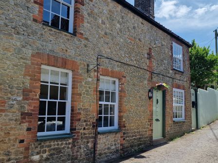 A stone cottage with white-framed windows and a light green door with flowers above the entrance at Granary Cottage in Warminster