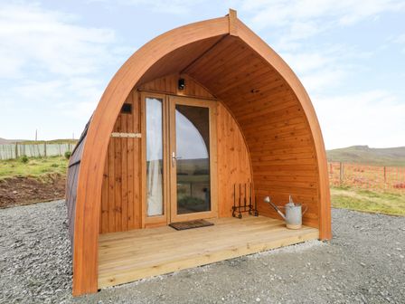 A wooden pod structure with a glass door and small porch area with a watering can at Garraidh Ghorm Pod in Conista
