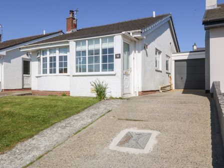 A single story white house with a driveway a front lawn and a garage at Sisial-Y-Mor in Rhosneigr