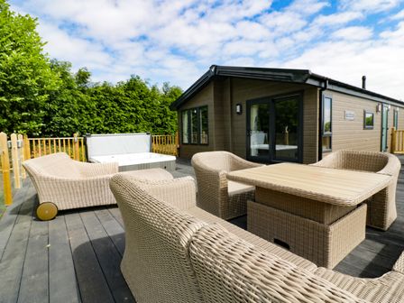 An outdoor patio deck with wicker furniture and a hot tub near a cabin at Pinehurst Lodge in St Day