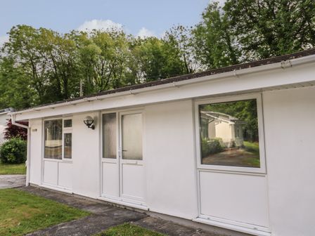 The exterior of a white single-story building with multiple windows and a door surrounded by trees at 11 Tremore in Liskeard