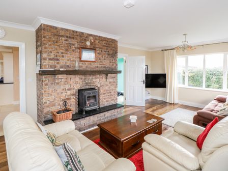 A living room with a brick fireplace white leather sofas wooden coffee table and a large window at Clifftop Haven in Tully Cross near Tully County Galway