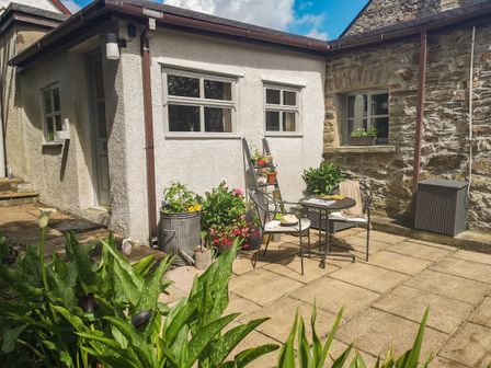 A small patio area with two chairs and a round table surrounded by potted plants outside a building with white and stone walls at The Byre in Dulas