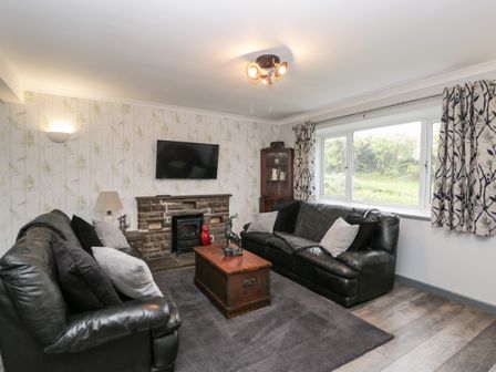 A living room with two black leather sofas a wooden chest coffee table and a wall mounted tv at Pool House The Narth near Trellech
