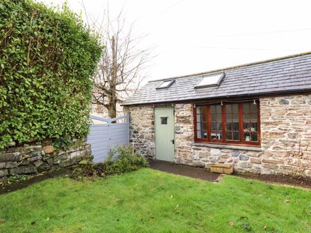 A stone cottage with a green door and wooden windows in a garden with grass and a hedge at Little Orchard Barn in St Austell