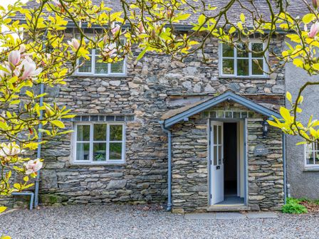 Stone house facade with windows and open door framed by branches with yellow leaves and flowers at Grassholme in Hawkshead
