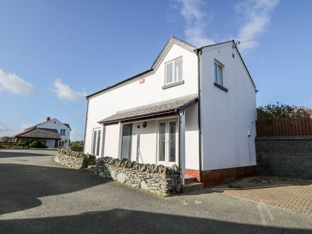 A two storey white house with stone wall and driveway under blue sky at Bay View in Trearddur Bay