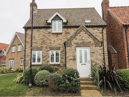 The front view of a brick house with white door and windows surrounded by bushes and a lamp post at Causeway Cottage in Filey