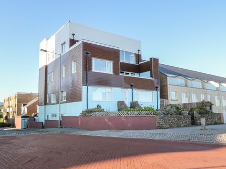 A multi-story residential building with brown and white siding and windows on a street corner at Sea View Apartment in Pwllheli