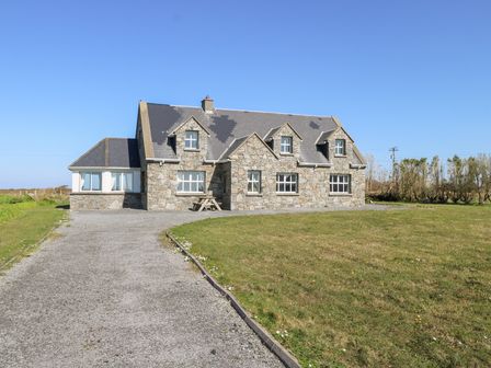 A stone house with multiple windows and a gravel driveway surrounded by grass at Realt na Maidne in Claddaghduff County Galway