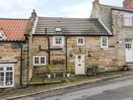 Stone exterior of a cottage with a cream door potted plants and hanging baskets at Willow Nook in Glaisdale near Lealholm