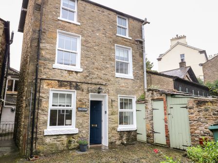 Stone exterior of a cottage with white-framed windows and a blue door next to green wooden sheds at Pine Cottage in Sedbergh