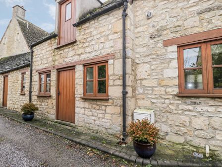 Exterior view of a stone cottage with wooden doors and windows and two potted plants outside at Chapel Cottage Leonard Stanley near Kings Stanley