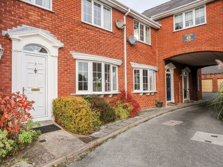Exterior view of red brick terraced houses with white framed windows and doors and small bushes along the walkway at Sea View Cottage Menai Bridge