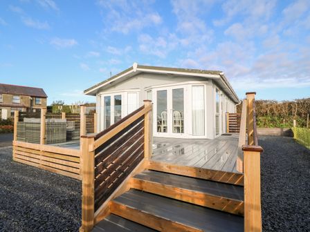 Exterior view of a single story building with a wooden deck and stairs leading up to glass doors at Caban Tywod in Abersoch