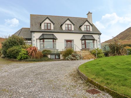 A two-story house with dormer windows a gravel driveway and shrubs at Starbay House in Eyeries County Cork