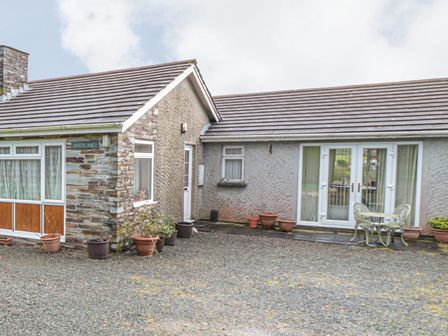 The exterior of a one-story house with several potted plants and a small metal table with two chairs on a stone patio at Little Lanes in Boscastle