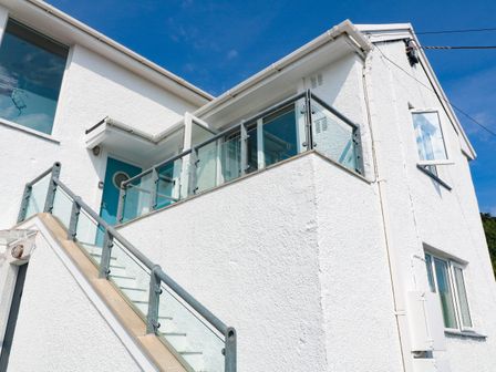 An exterior view of a white building with a staircase and a balcony with glass railings at The Poop Deck in Coverack