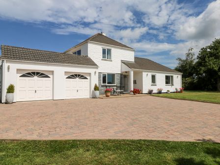A white two-story house with a double garage a paved driveway and potted plants at Trevore Farmhouse in Chacewater