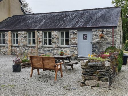 A stone cottage with wooden bench and table outside and flower beds at Mimi's Cottage in St Neot
