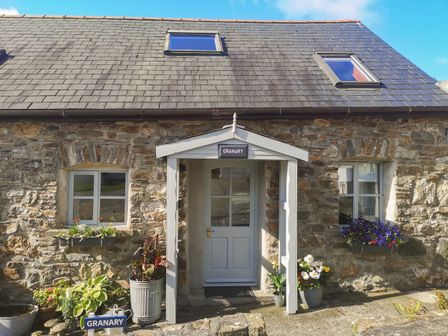 Front view of a stone house with a white door and two windows with flower boxes at The Granary in Dulas