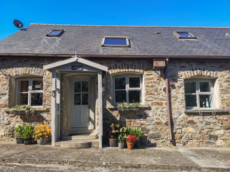 Stone house exterior with three windows and a door with porch and plants at The Stables in Dulas