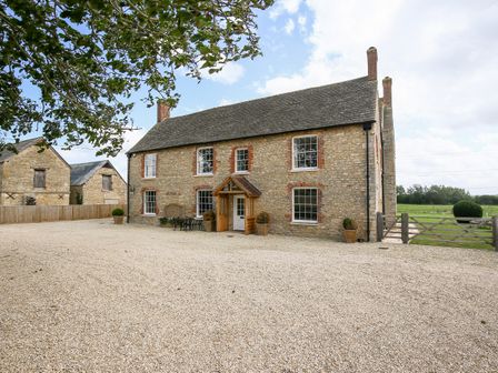 A stone farmhouse with white framed windows and wooden porch on a gravel driveway at Shifford Manor Farm in Shifford near Bampton Oxfordshire
