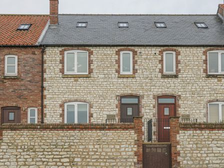A stone cottage with a brick wall and two wooden doors at East Newk Cottage in Flamborough