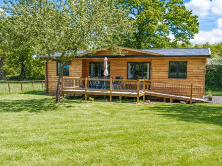 A wooden cabin with a deck and outdoor furniture surrounded by grass and trees at Top Style Orchard in Hallow