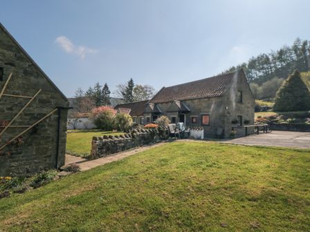 A stone house with a tiled roof surrounded by grass and trees at Rosedale in Glaisdale