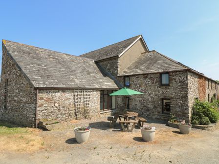 A stone building with a slate roof and outdoor picnic table with green umbrella and flower pots at The Roundhouse in Bude