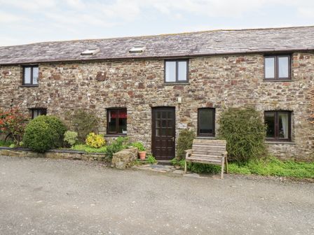 Stone cottage exterior with wooden door bench and garden beds at Swallow Cottage in Bude