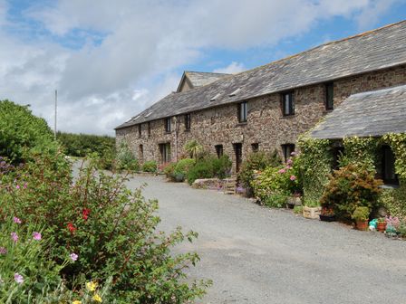 A stone building with a slate roof and plants along a gravel driveway at The Wagon Linney in Bude
