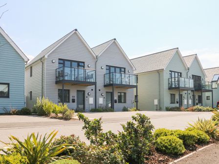 A row of modern two-story houses with balconies and glass railings surrounded by plants and bushes at Devonair in Westward Ho
