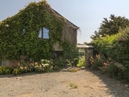 A gravel driveway leading to a house covered in ivy with flower beds and an archway to a garden at The Stable in Bude