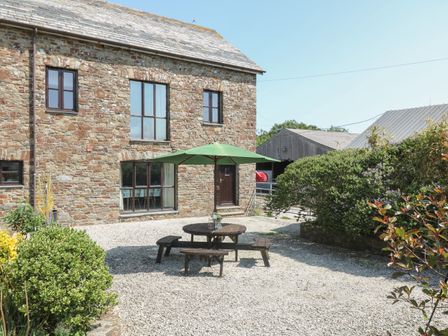 A stone house with a patio table and green umbrella on gravel outside at The Dairy in Bude