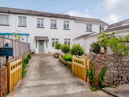A driveway with small trees and plants on each side leading to a white two-story house with a green door and windows at Martingale in Torquay