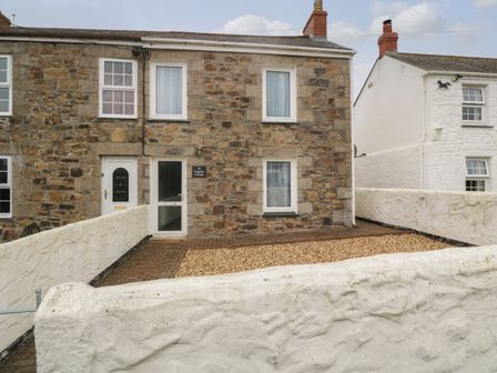 A stone fronted house with white framed windows and doors behind a white painted stone wall at Nappers Cottage in Connor Downs