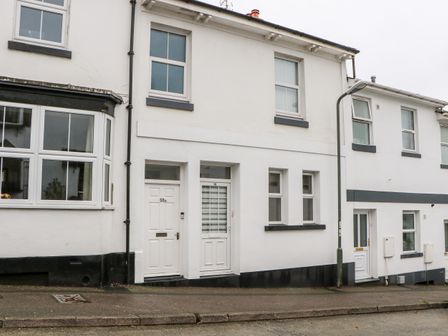 Front view of a row of white terraced houses with multiple windows and doors on a street with a sidewalk and a street light at Cove Cottage in Torquay