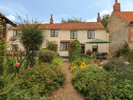 A garden path leading to a cream cottage with red roof tiles and an outdoor seating area with umbrella at Primrose Cottage in Stiffkey