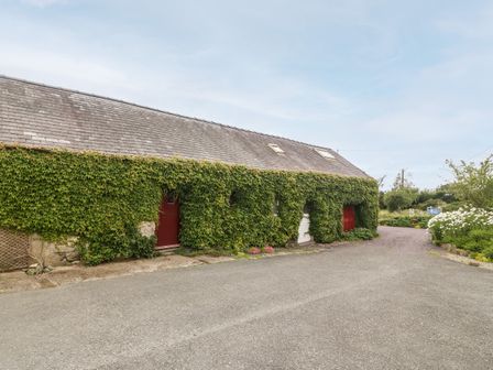 A building covered in ivy with multiple doors and a gravel driveway at Llofft Yr Yd in Llandwrog near Dinas Dinlle