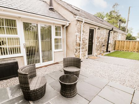 An outdoor patio with two wicker chairs and a wicker table on stone tiles at 2 Mountain View in Talwrn near Llangefni