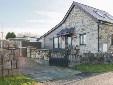 Stone house with a slate roof and black gate on a driveway at Ysgubor Ddegwm Bach in LLanddona near Beaumaris