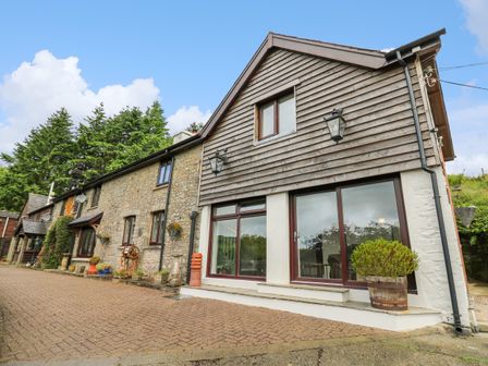 A stone and wood-sided house with large windows and potted plants outside at Cwmfadog in Llanafan-fawr near Beulah