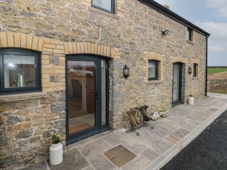 A stone exterior wall with glass doors windows and rubber boots on a stand at The Granary in St Brides Major