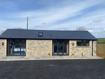 A stone building with a tiled roof and black framed windows and doors at The Cwtch in St Brides Major