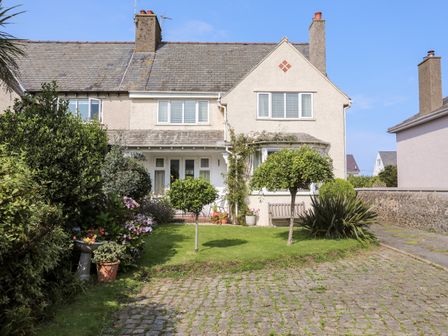 A two-story house with a tiled roof a small front garden with trimmed trees and flower pots and a cobblestone driveway at Afallon in Nefyn