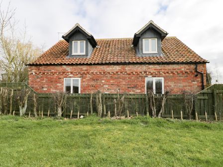 A brick house with two dormer windows and a tiled roof behind a wooden fence and small leafless trees at Pipistrelle Cottage in Brandesburton